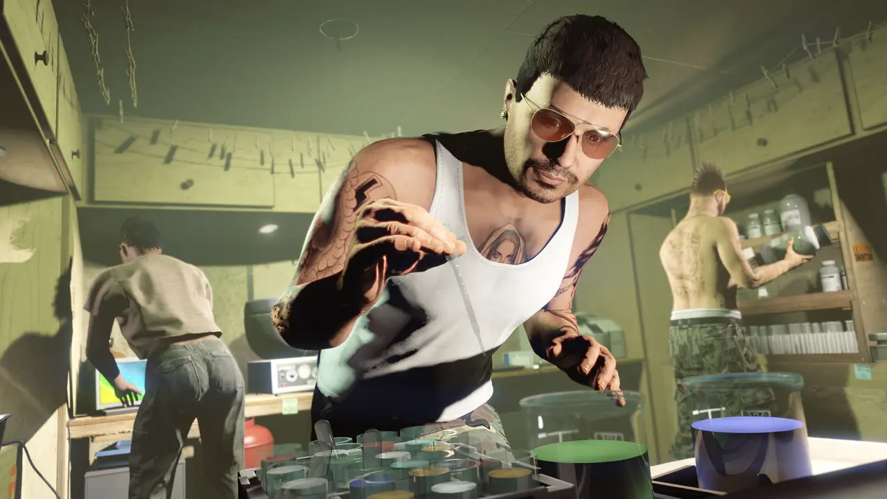 Un personnage de GTA Online en marcel blanc, lunettes de soleil et bras tatoués, manipule une pipette au-dessus d'un rack d'échantillons chimiques colorés dans un laboratoire de fortune, deux comparses s'affairant autour