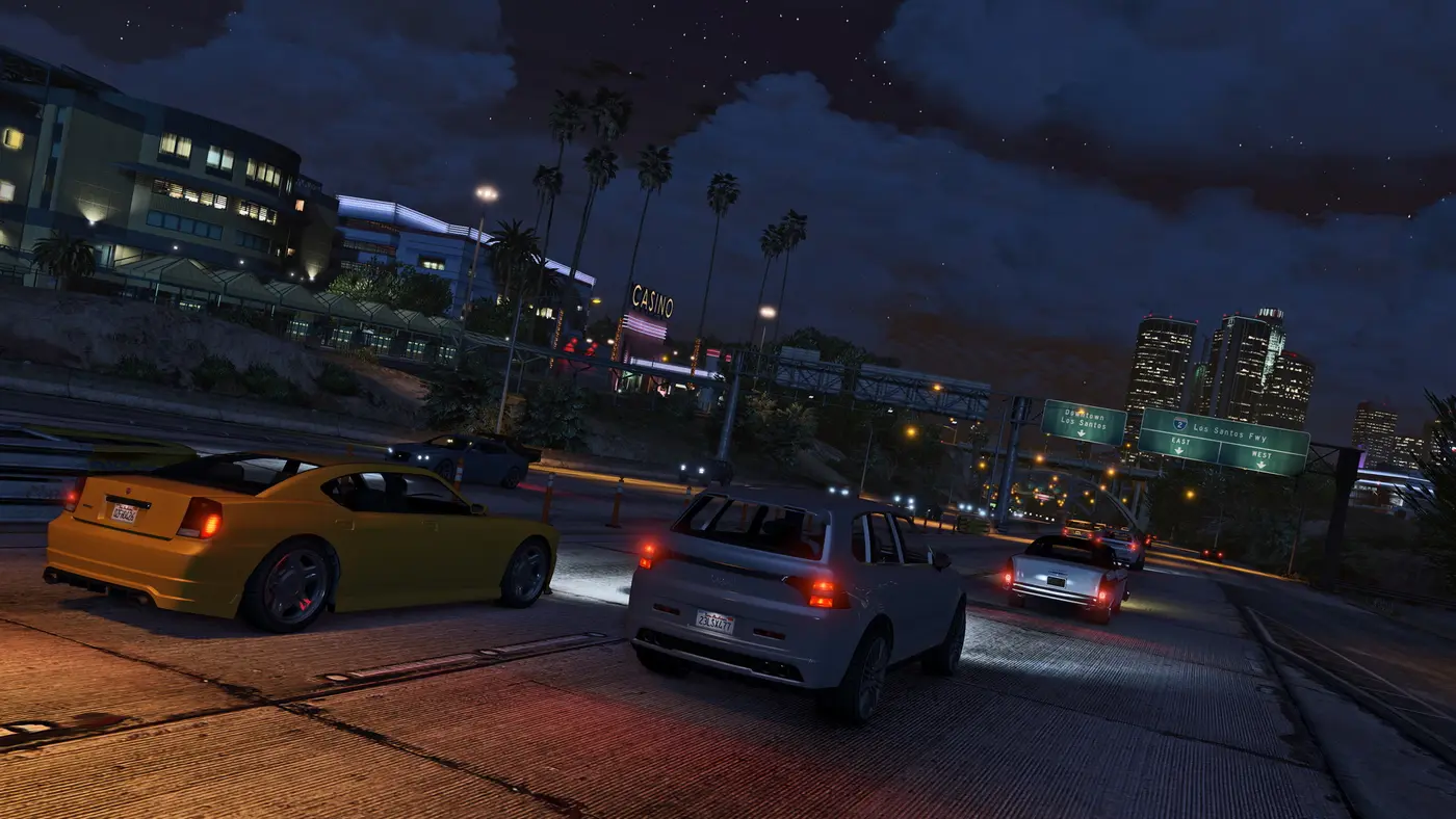 Los Santos de nuit dans GTA 5, une autoroute urbaine, l'enseigne d'un casino et les gratte-ciel du centre-ville éclairés au loin sous un ciel étoilé