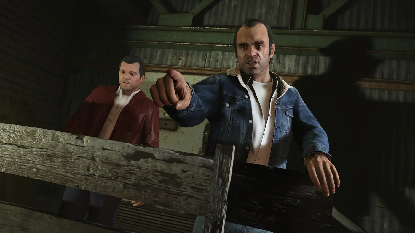 Michael De Santa en veste de cuir rouge à gauche et Trevor Philips en veste de jean pointant du doigt à droite, dans un hangar de GTA V